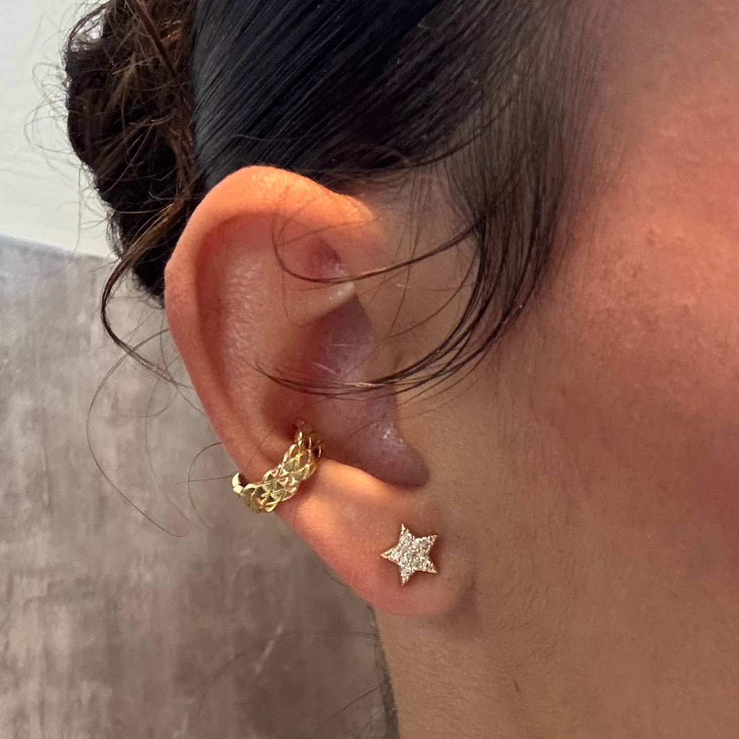 Close-up of an ear wearing gold and silver star-shaped earrings with a neutral background.